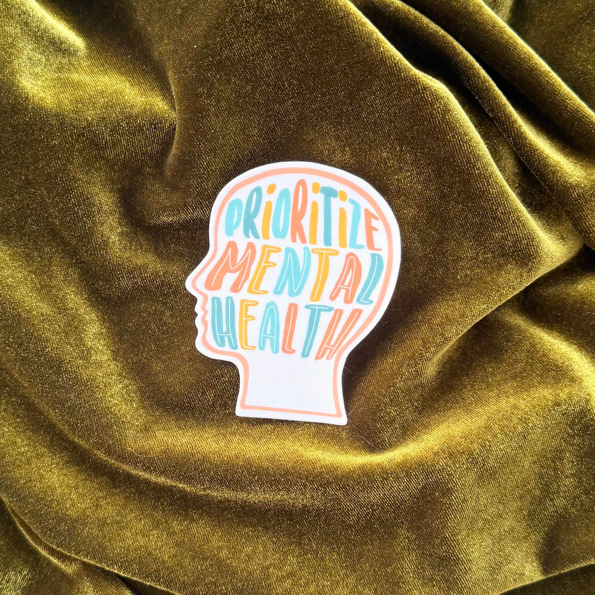 Sticker with 'Prioritize Mental Health' text on a textured green fabric background